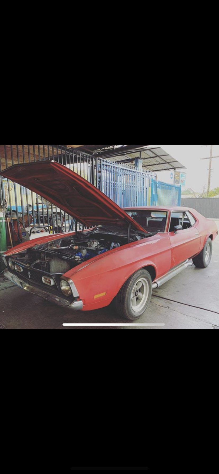 Red classic Ford Mustang with open hood undergoing engine repair in an auto workshop