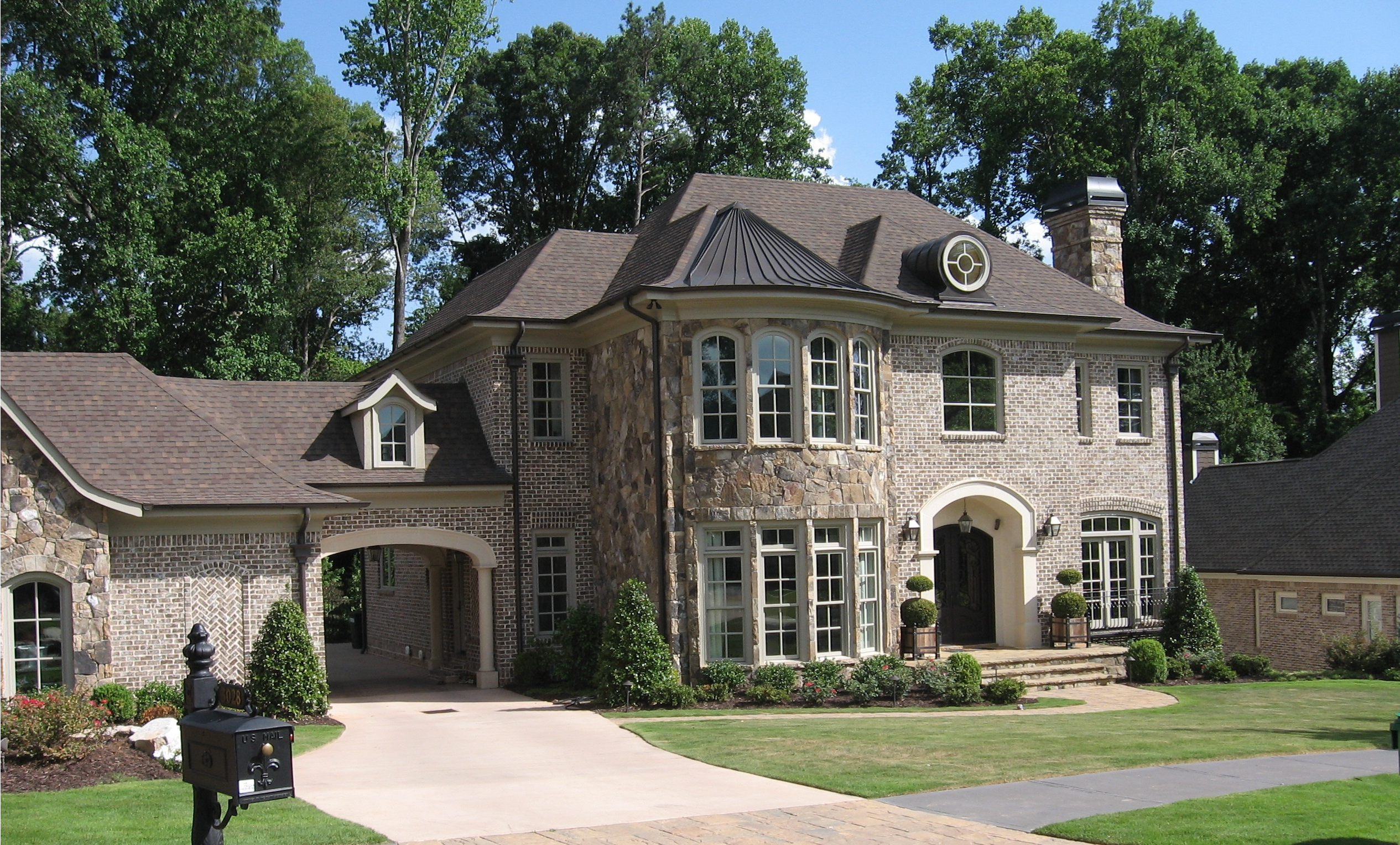 Elegant two-story brick house with stone accents, surrounded by well-manicured lawn and trees.