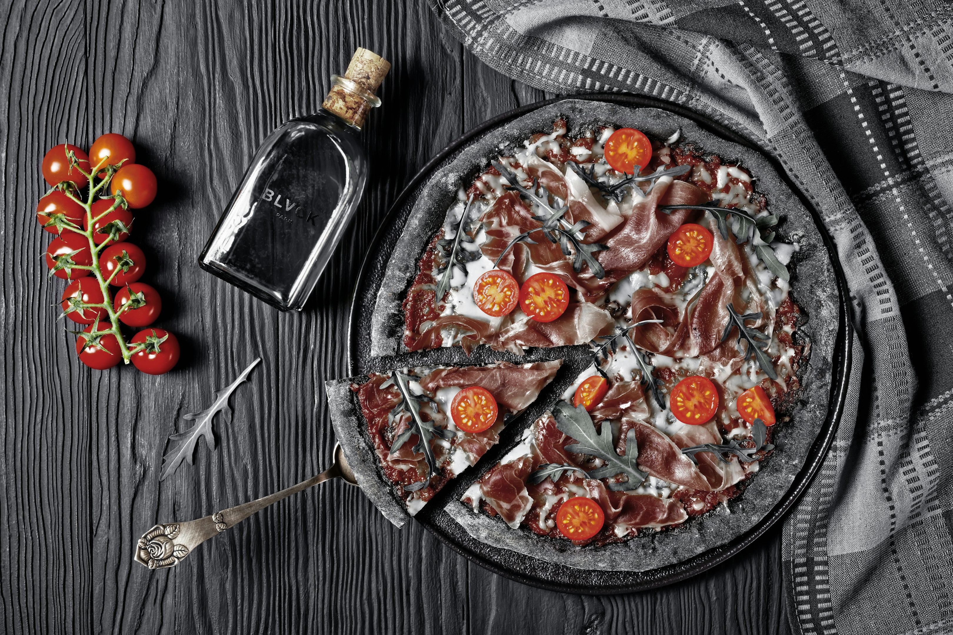 pizza en plato de cerámica negro redondo al lado de tenedor y cuchillo plateados