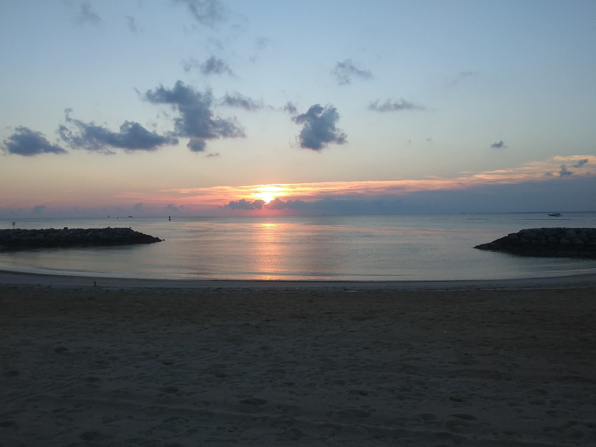 Sunset over calm ocean beach with colorful sky, scattered clouds, and rocky breakwaters