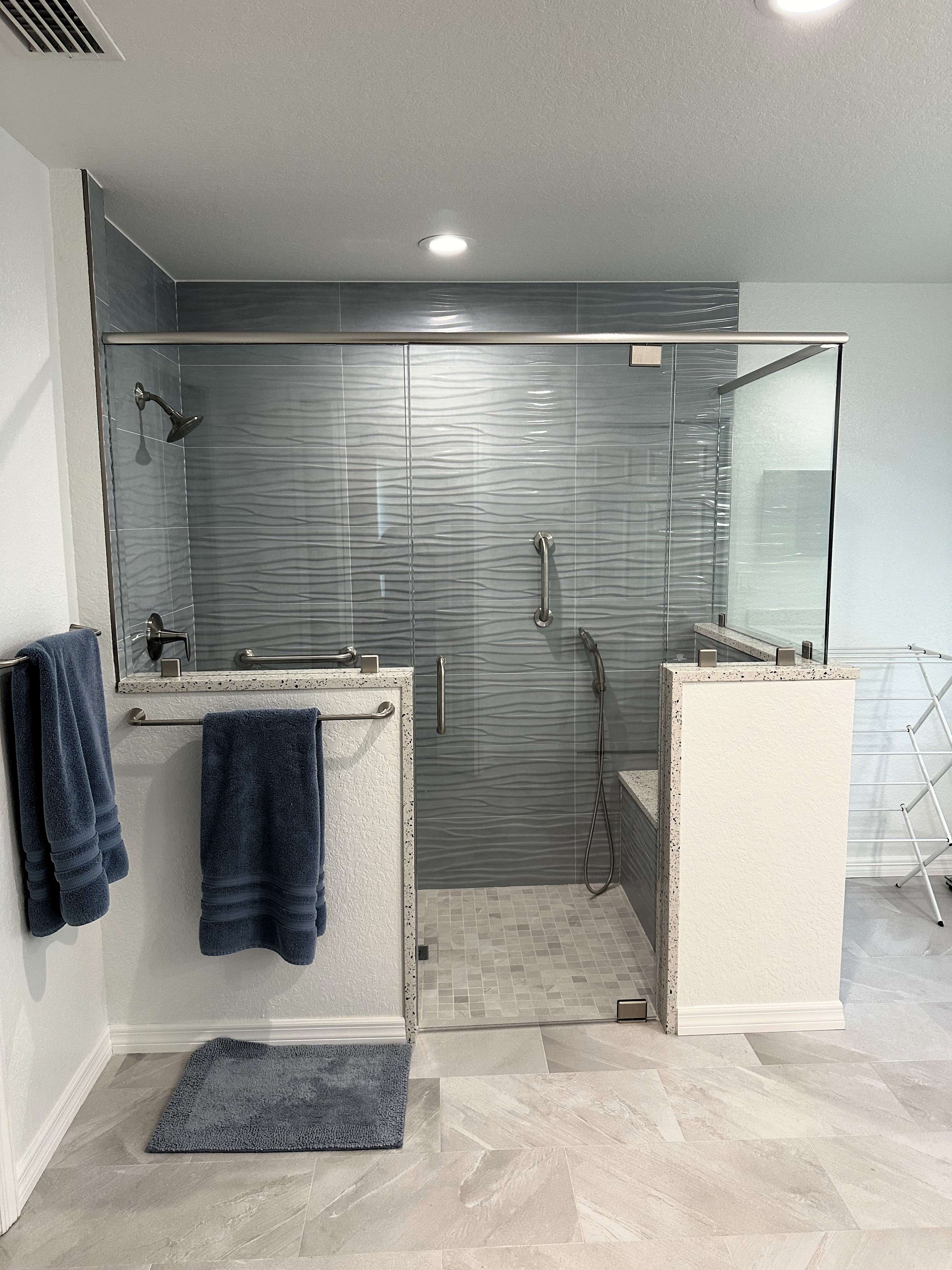 Large coastal tiled walk-in shower featuring striking 12x36 aqua-colored wavy wall tile and soft grey 2x2 matte shower floor with 3/8" heavy clear glass door and panels.