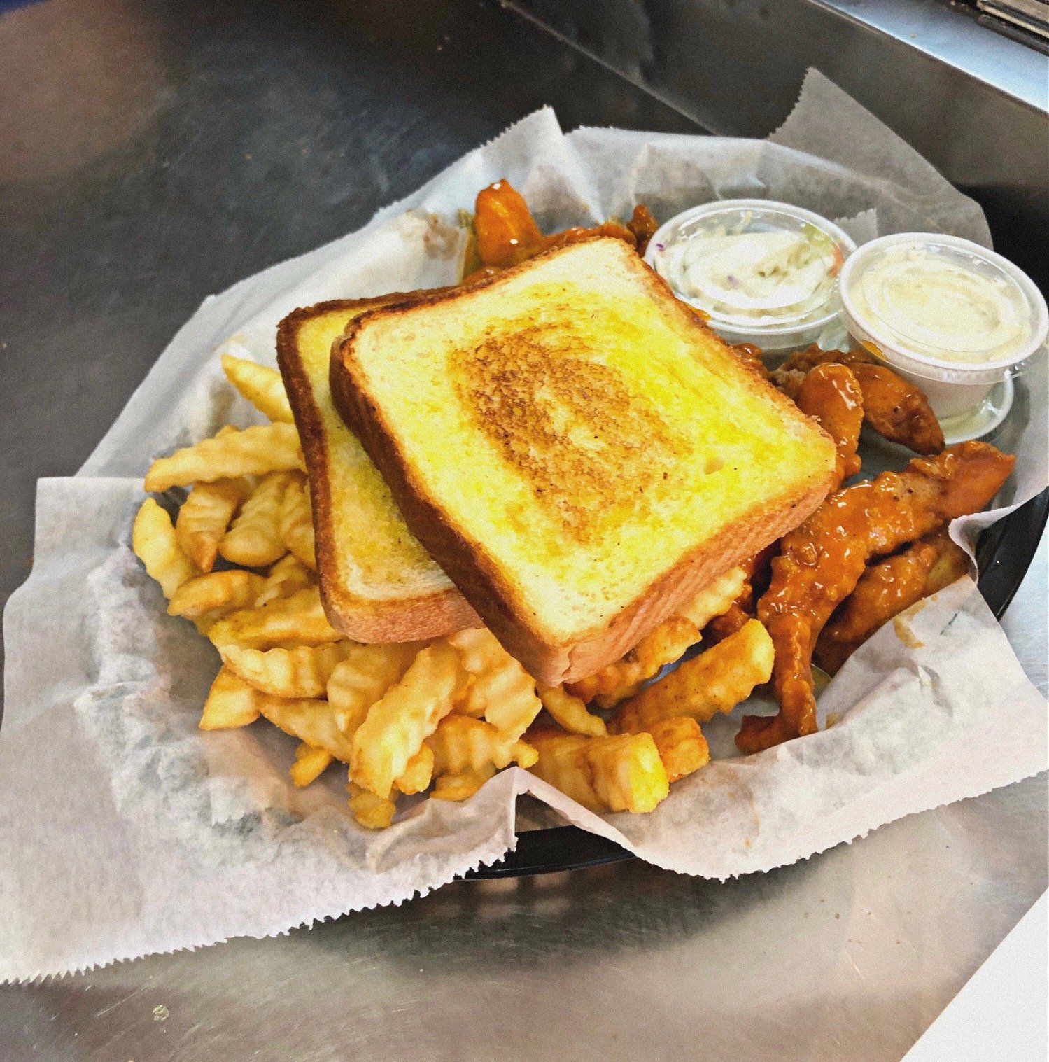 Plate of crinkle-cut fries, buffalo chicken tenders, two slices of toasted bread, and dipping sauces on a lined tray.