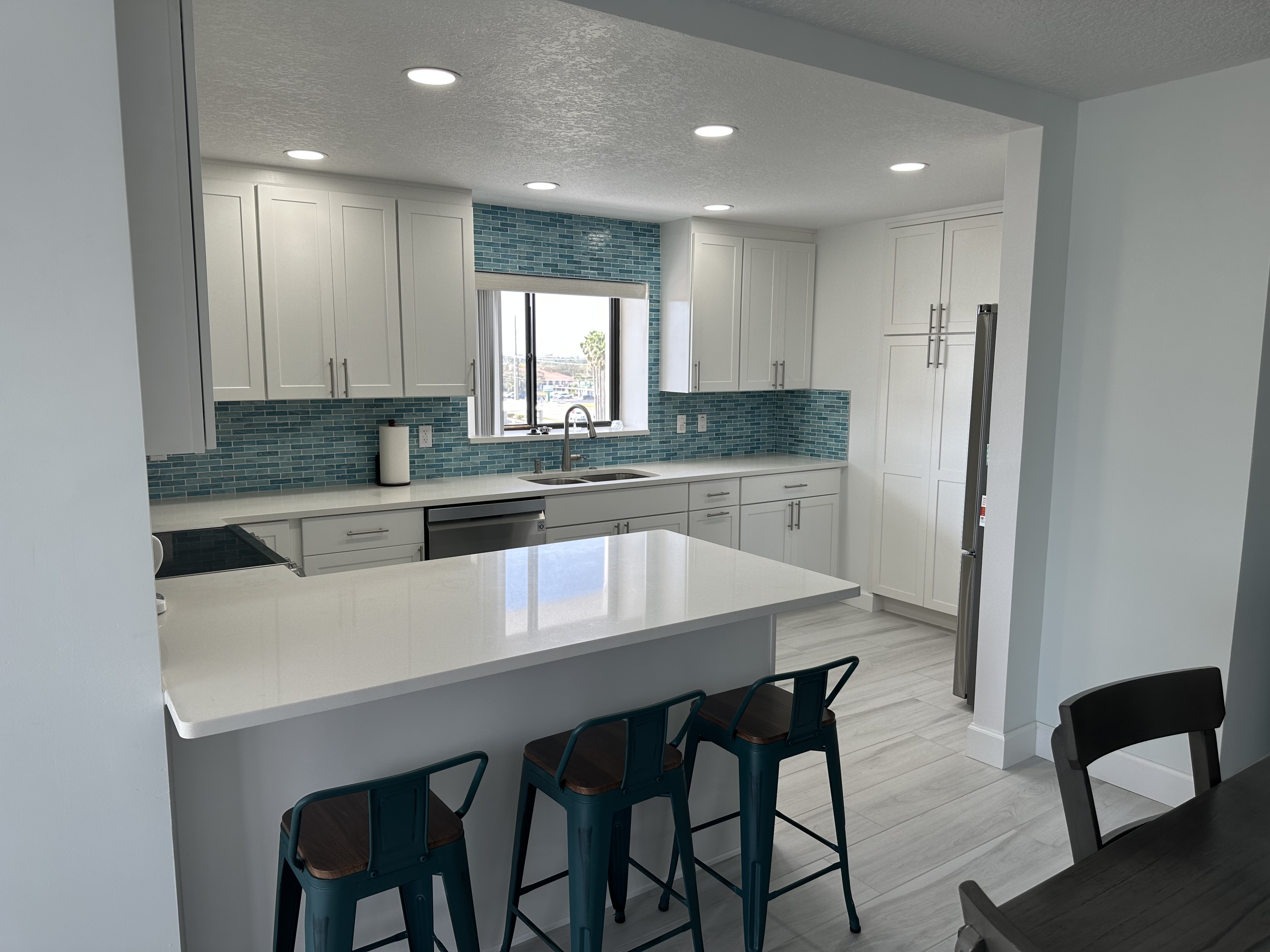 Coastal kitchen featuring painted white shaker cabinetry, hot blue backsplash, and white quartz countertops.