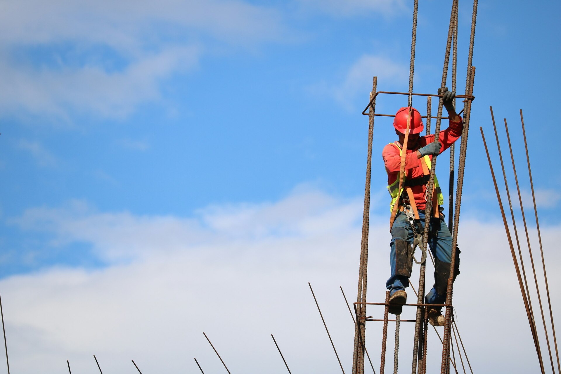 Construction worker on steel framework with safety gear against blue sky.