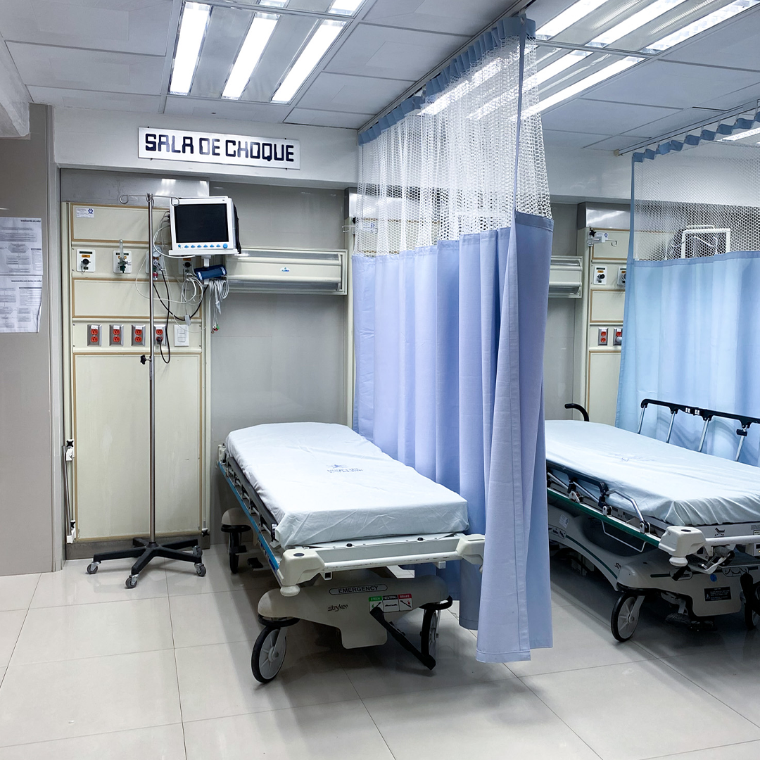 Dos enfermeras con mascarillas hablando en el pasillo de un hospital, llevando uniformes azules y estetoscopios.