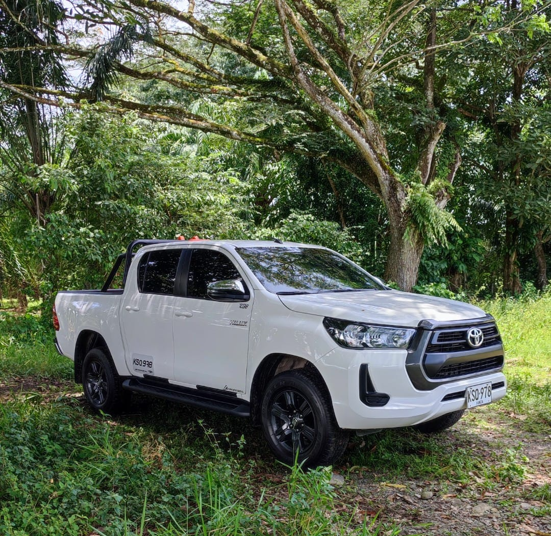 Camioneta pickup Toyota Hilux blanca estacionada en sendero rodeado de vegetación tropical Camioneta pickup Toyota Hilux blanca estacionada en sendero rodeado de vegetación tropical