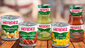 Cesta de frutas y verduras frescas con frascos de miel, pan, bollos y galletas sobre una mesa de madera en una tienda de comestibles.