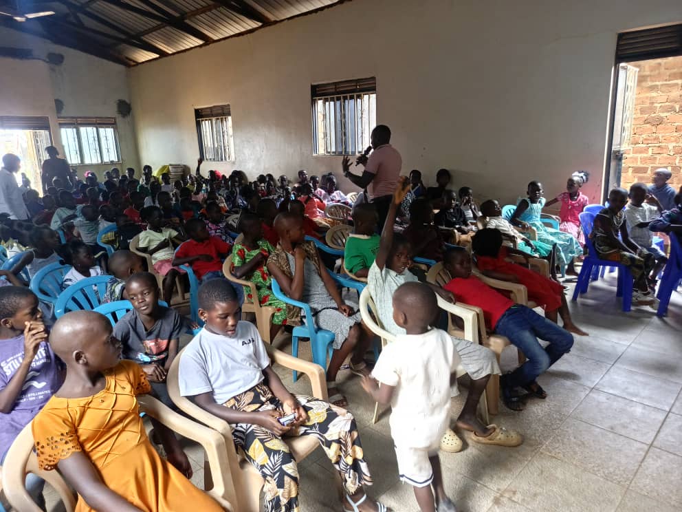 Children playing and holding hands with adults under a tent during a community event in a rural setting.