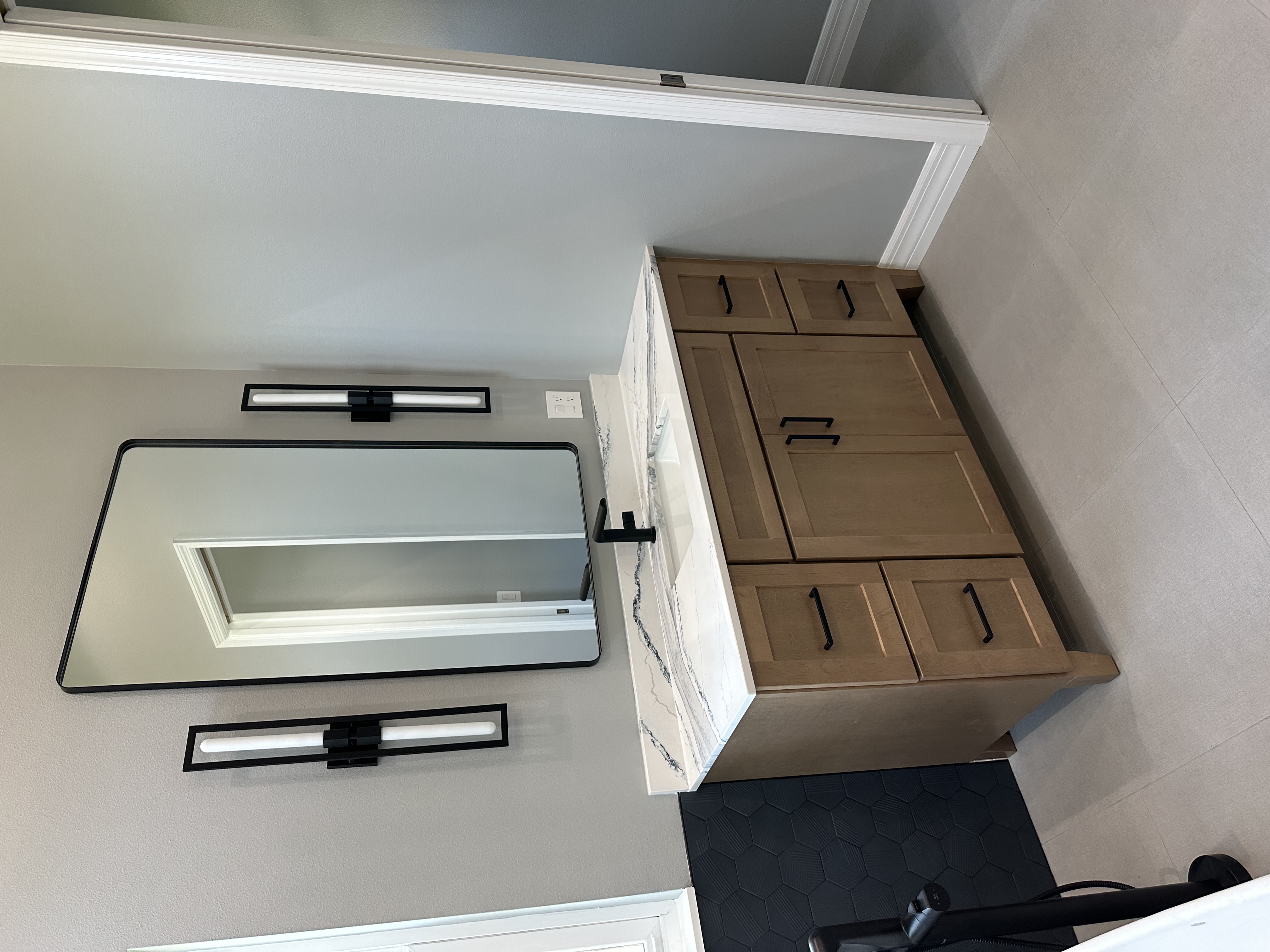 This chic primary bathroom showcases semi-custom Biscotti-stained cabinetry, matte black fixtures, and 
a striking Cambria Hi-Gloss Bristol Bay quartz countertop—blending warmth and modern elegance with high-end finishes.