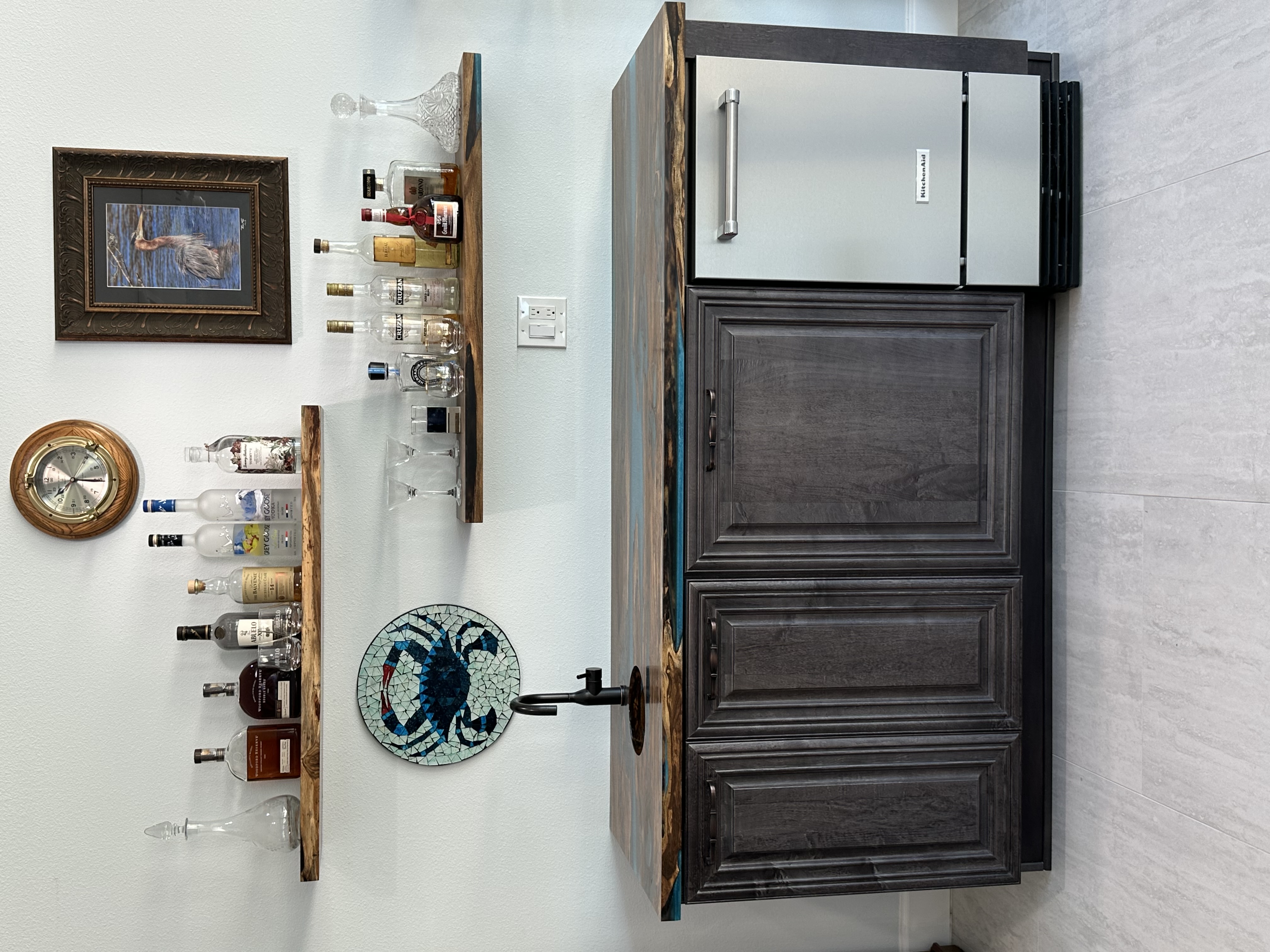 This timeless wet bar showcases semi-custom stained cabinetry and a striking live edge countertop, complemented by open shelving—creating the perfect setting for crafting an evening cocktail.