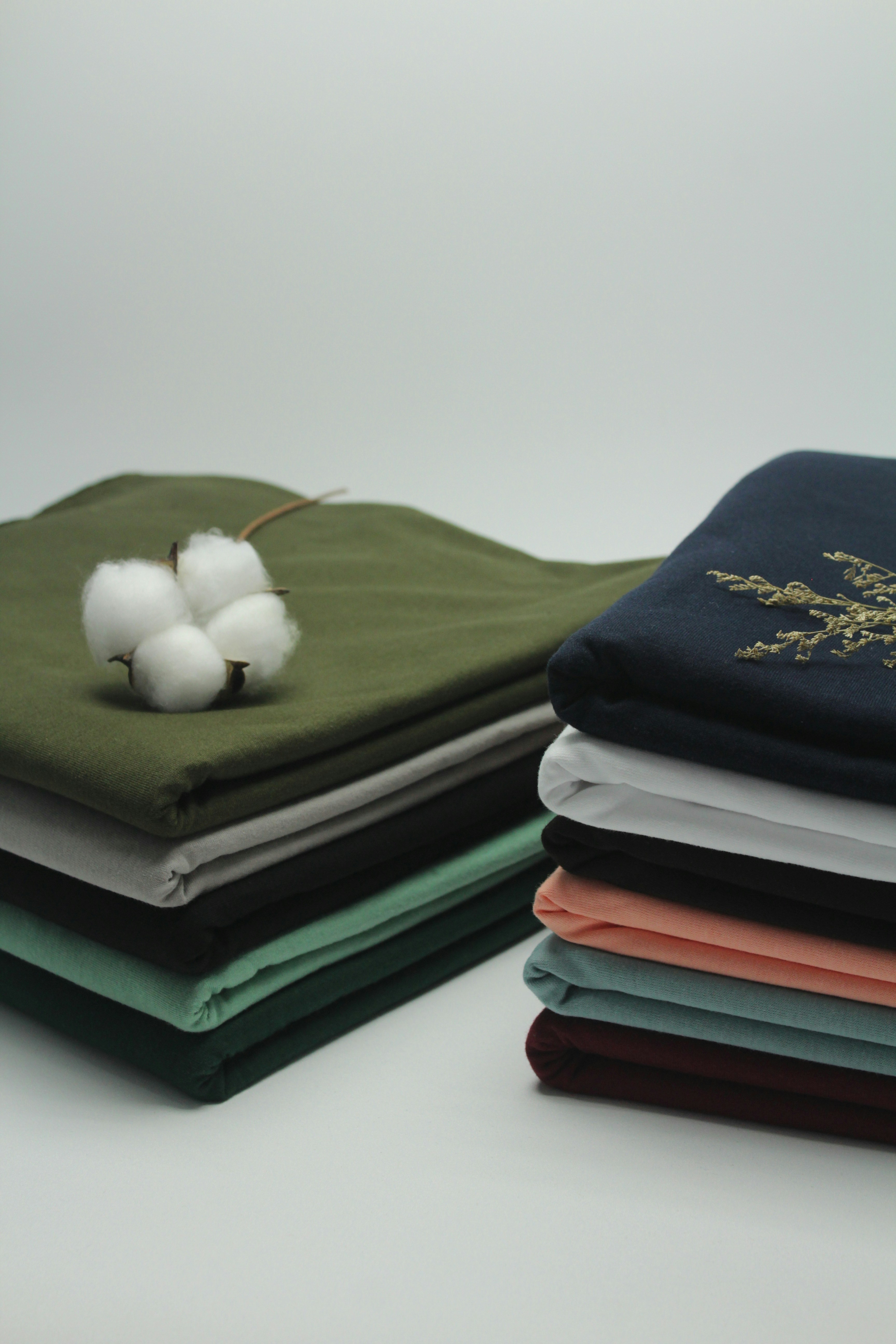 Ropa de algodón doblada en varios colores con flor de algodón natural sobre tela verde Ropa de algodón doblada en varios colores con flor de algodón natural sobre tela verde