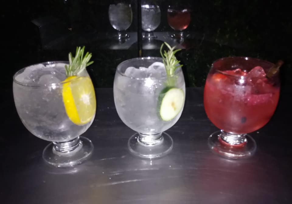 Tres copas de cócteles sobre una mesa, dos transparentes con rodajas de limón y pepino, y una roja con frutos rojos.