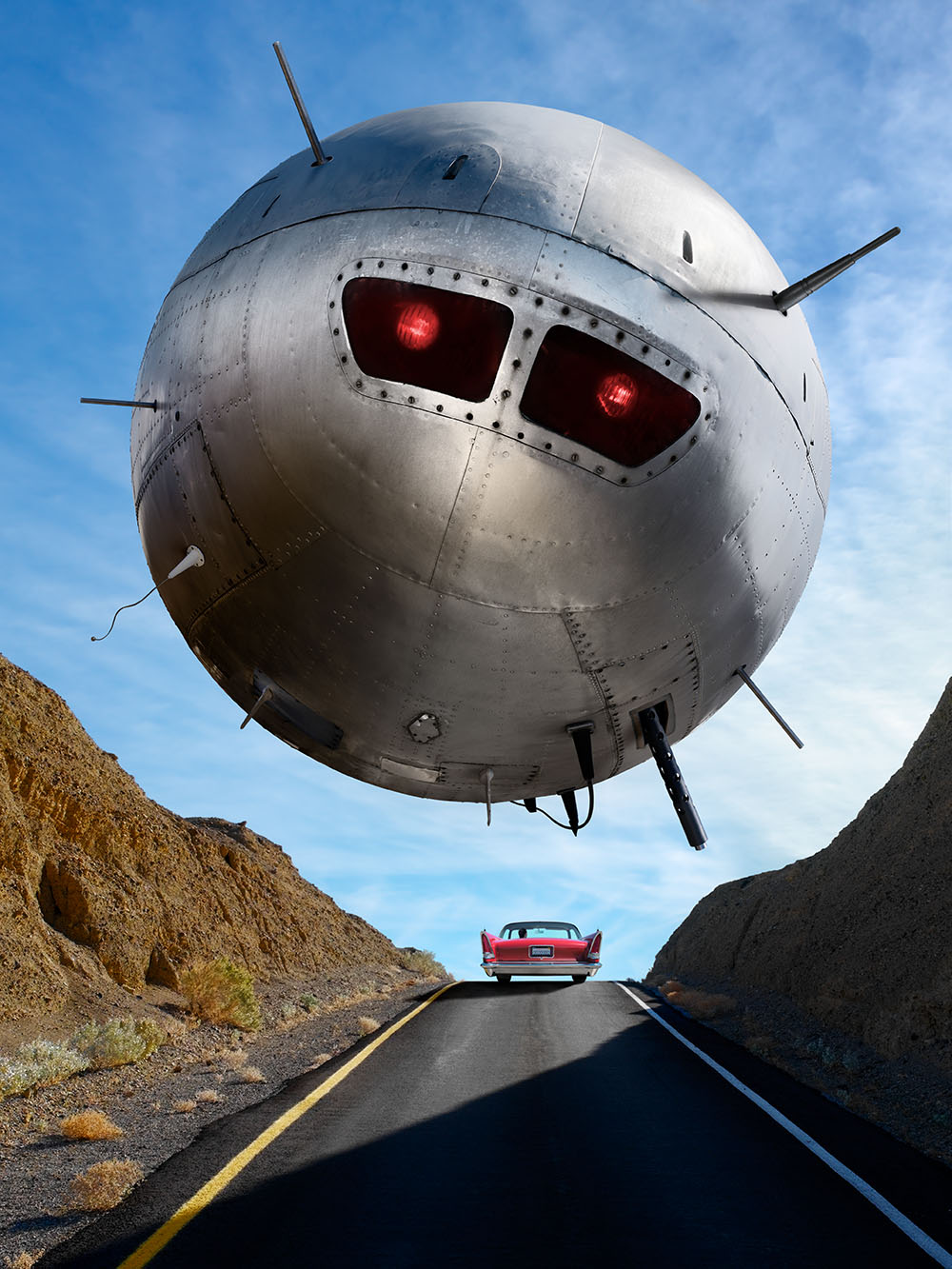 A spherical UFO flying over a highway, bristling with weapons and antenna. A vintage car is visible in the distance.