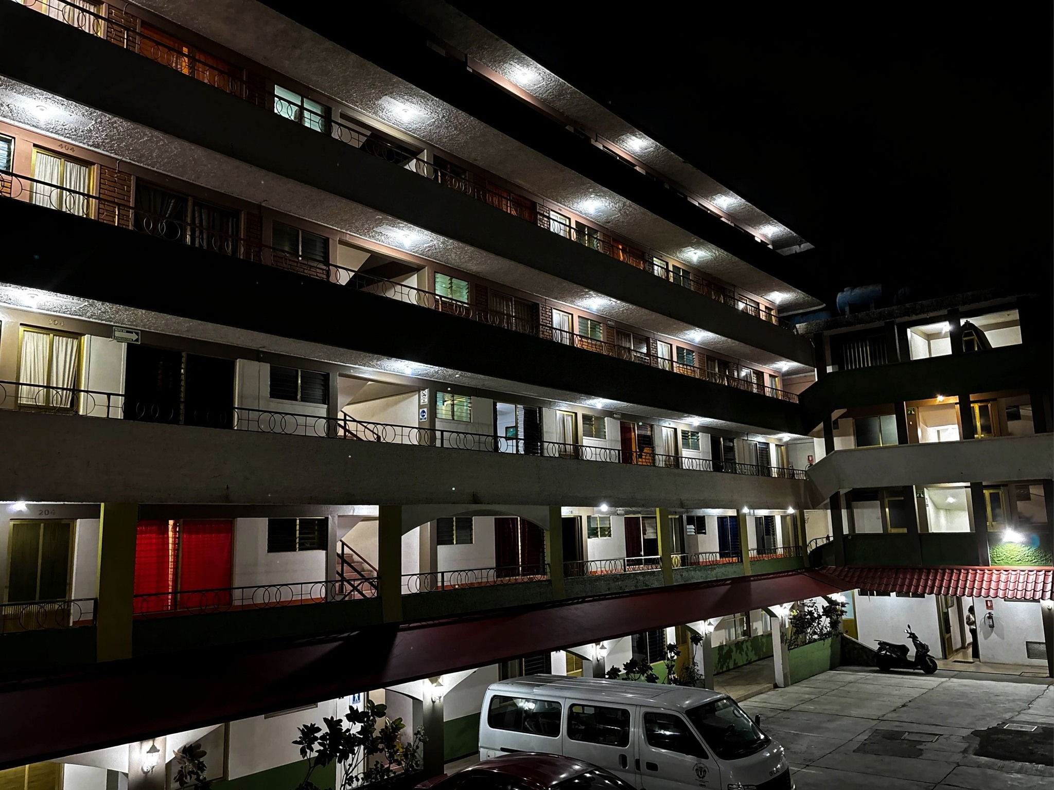 Dormitorio moderno con cama doble, plantas en macetas, iluminación colgante y grandes ventanales.