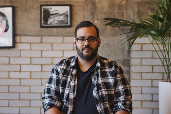 autorretrato de hombre usando camisa con botones de cuello gris y blanco cerca de planta de hojas verdes con maceta de cerámica blanca