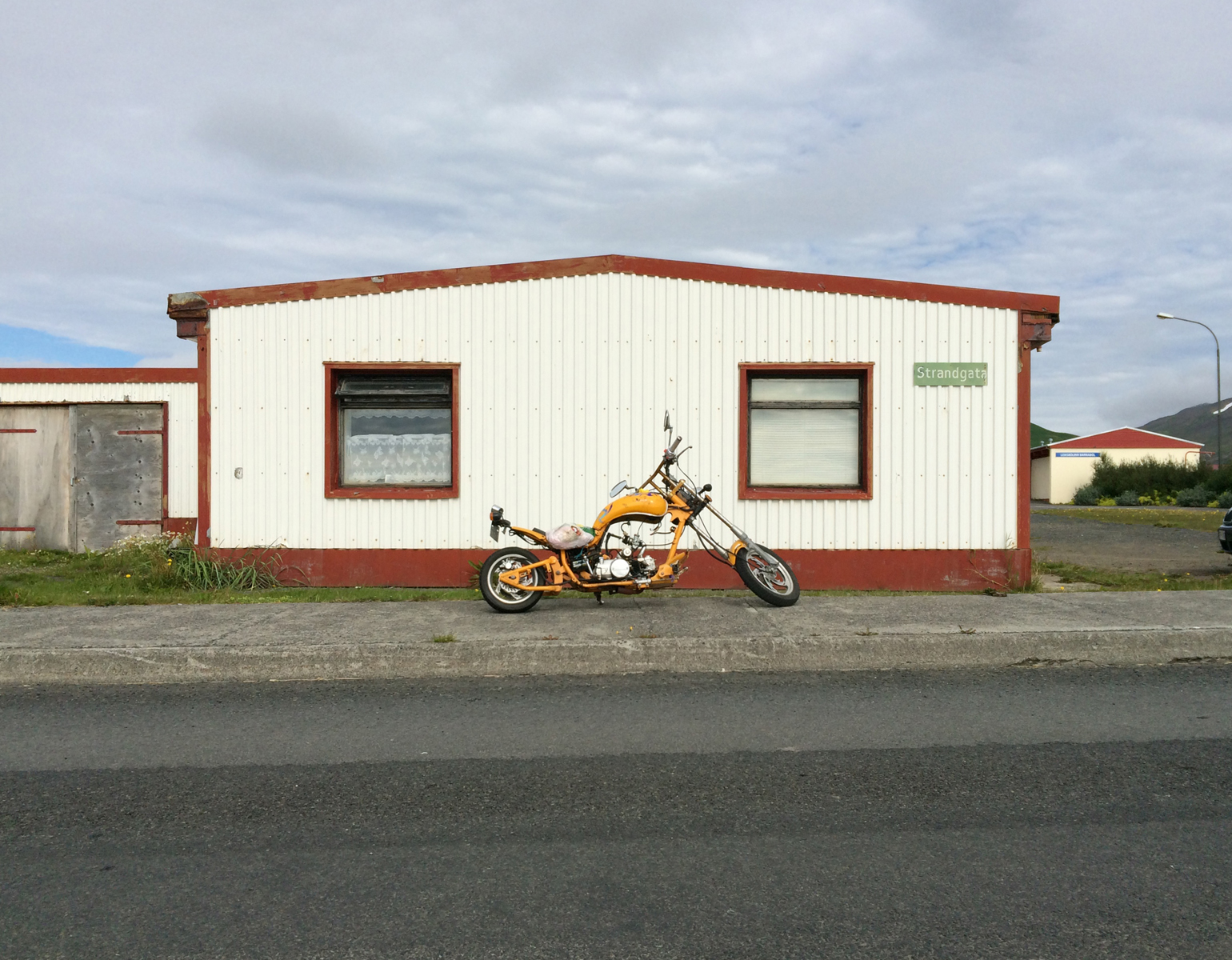 A white metal house with red trim, a yellow chopper motorcycle parked in front.