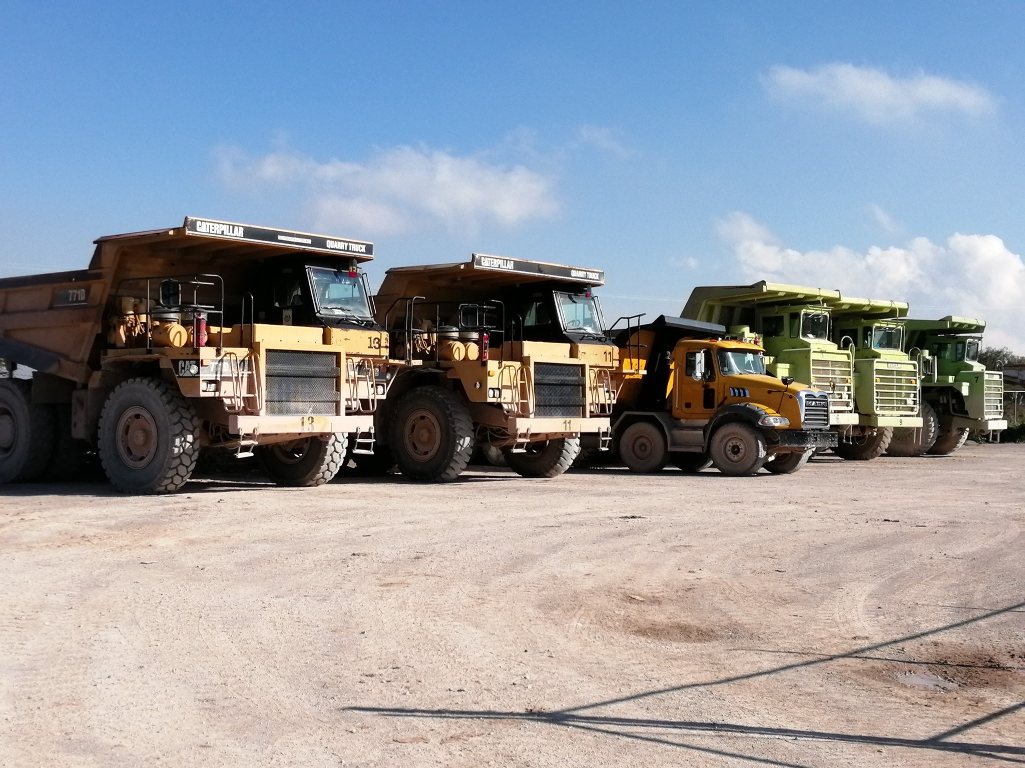 Camiones de carga pesados alineados en un sitio de construcción bajo un cielo despejado. Camiones de carga pesados alineados en un sitio de construcción bajo un cielo despejado.