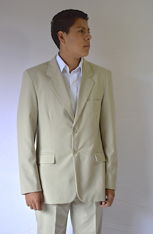 Persona con camisa azul y delantal negro en un pasillo con piso de baldosas grises y planta decorativa.