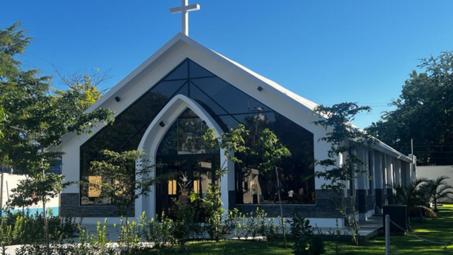 Fachada de iglesia moderna con cruz blanca, rodeada de árboles y césped, cielo azul despejado. Fachada de iglesia moderna con cruz blanca, rodeada de árboles y césped, cielo azul despejado.