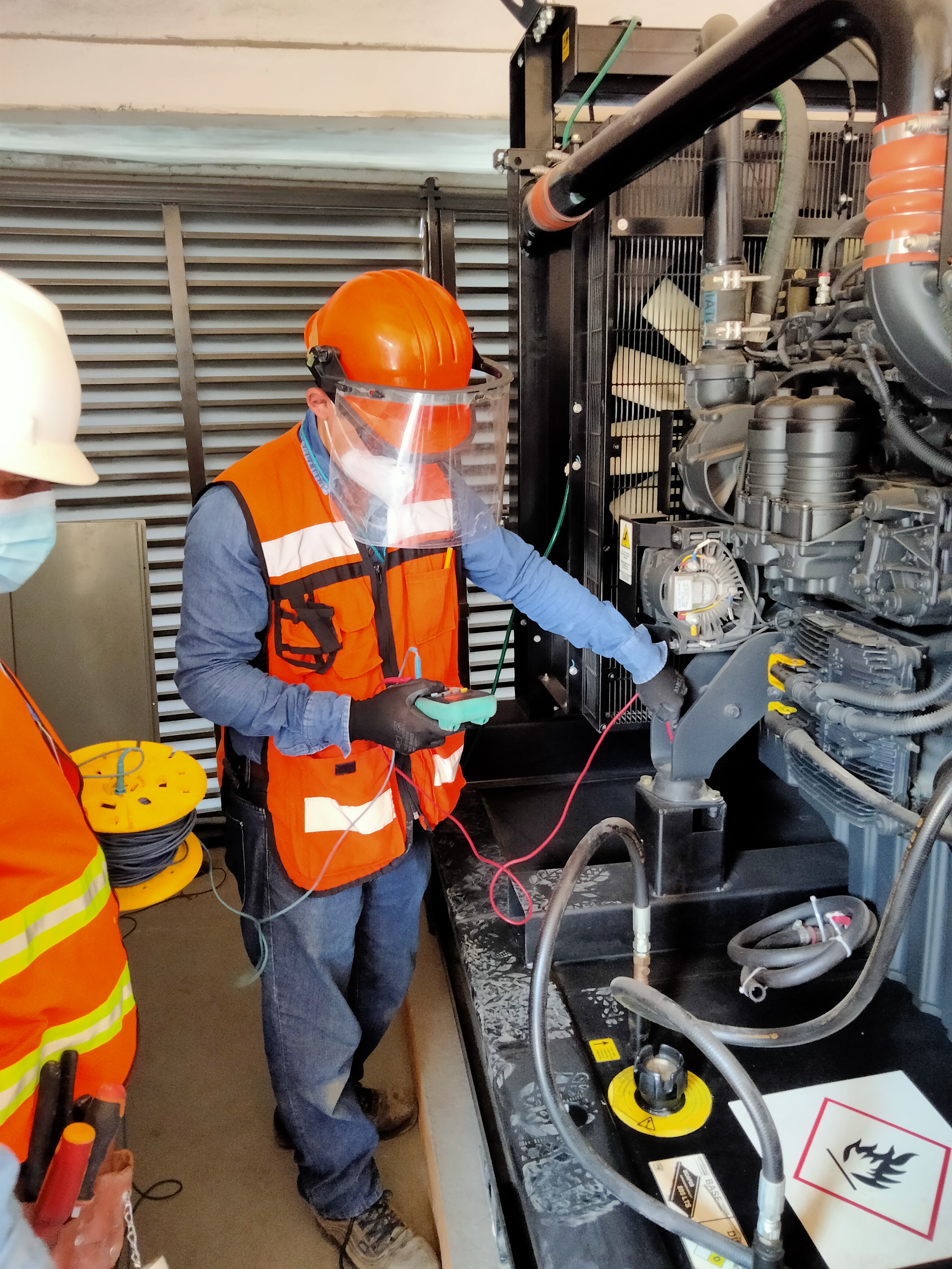 Técnico con casco y equipo de protección revisando un generador industrial.