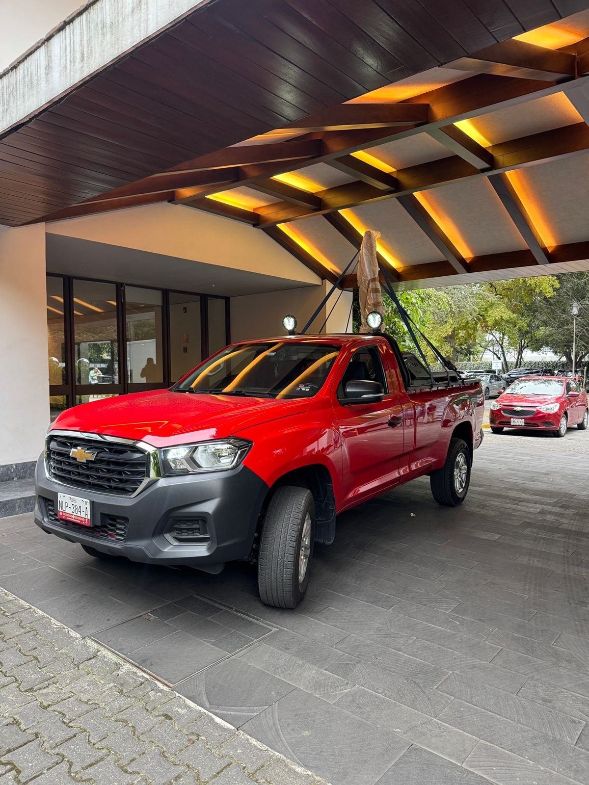 Red Chevrolet pickup truck parked under modern wooden awning with illuminated ceiling.