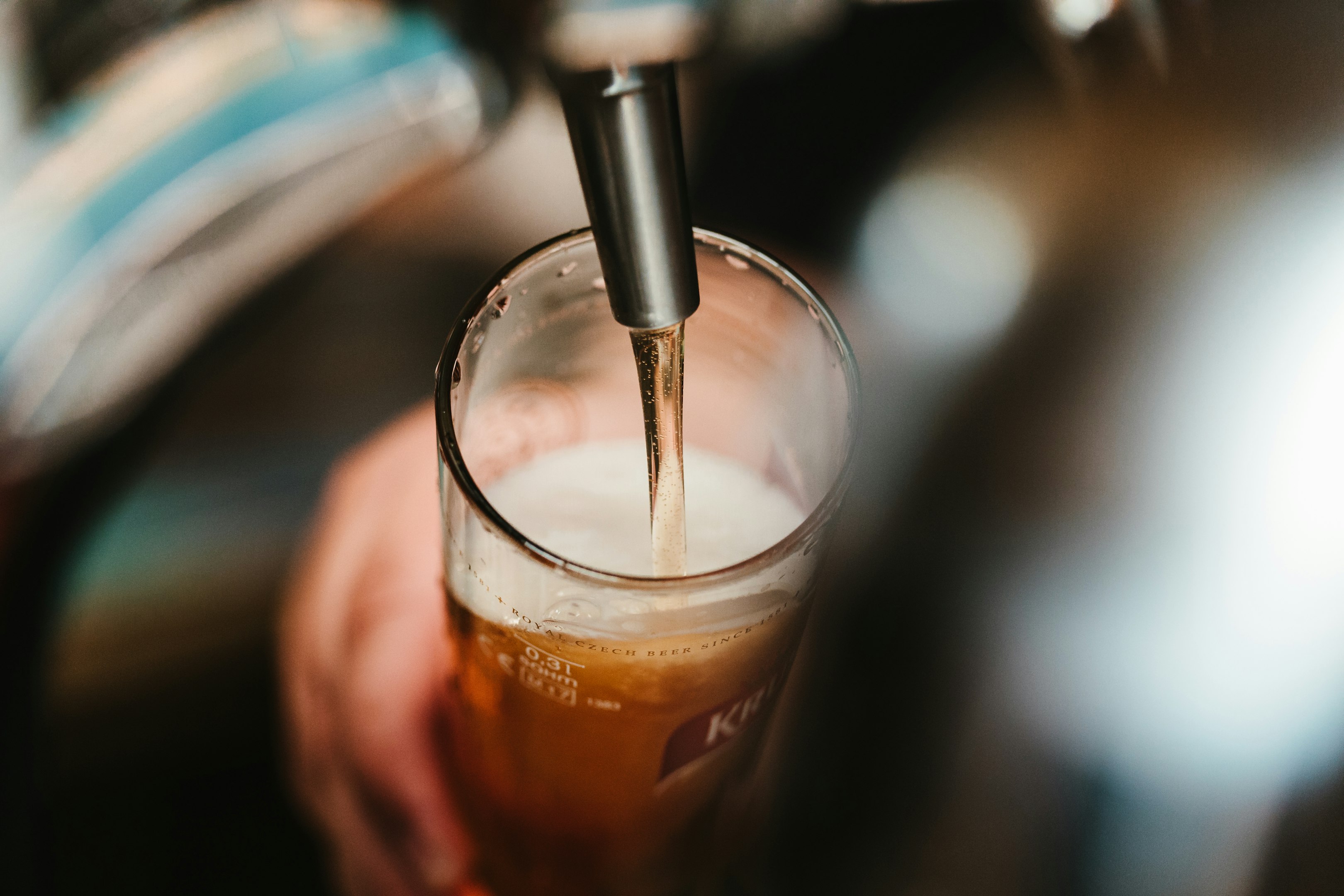 Vaso de cerveza dorada con espuma en un ambiente de bar acogedor, con luces cálidas y mesas de madera.