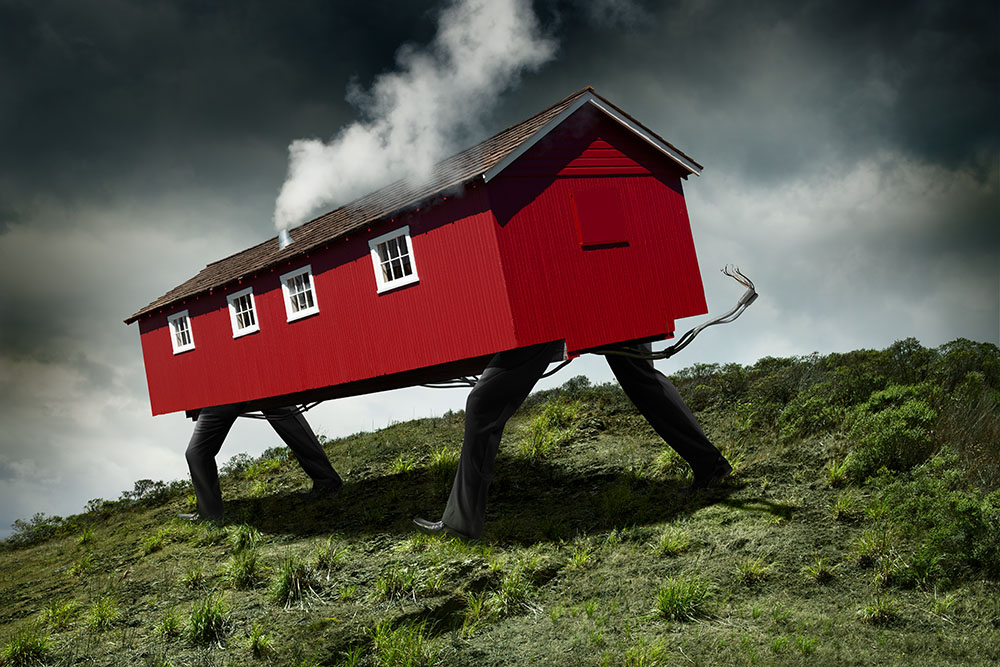Magical realist image of a house with four legs marching down a hillside, as white smoke billows from its chimney. 