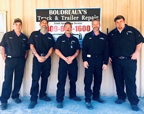 Five mechanics in black uniforms standing in front of Boudreaux's Truck & Trailer Repair sign.