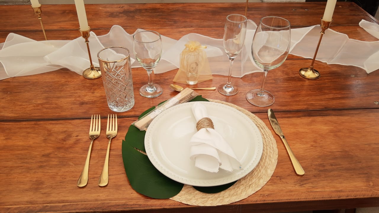 Mesa de comedor elegantemente decorada con cubiertos dorados, copas de cristal, platos blancos sobre hojas verdes y servilleta blanca en anillo. Mesa de comedor elegantemente decorada con cubiertos dorados, copas de cristal, platos blancos sobre hojas verdes y servilleta blanca en anillo.