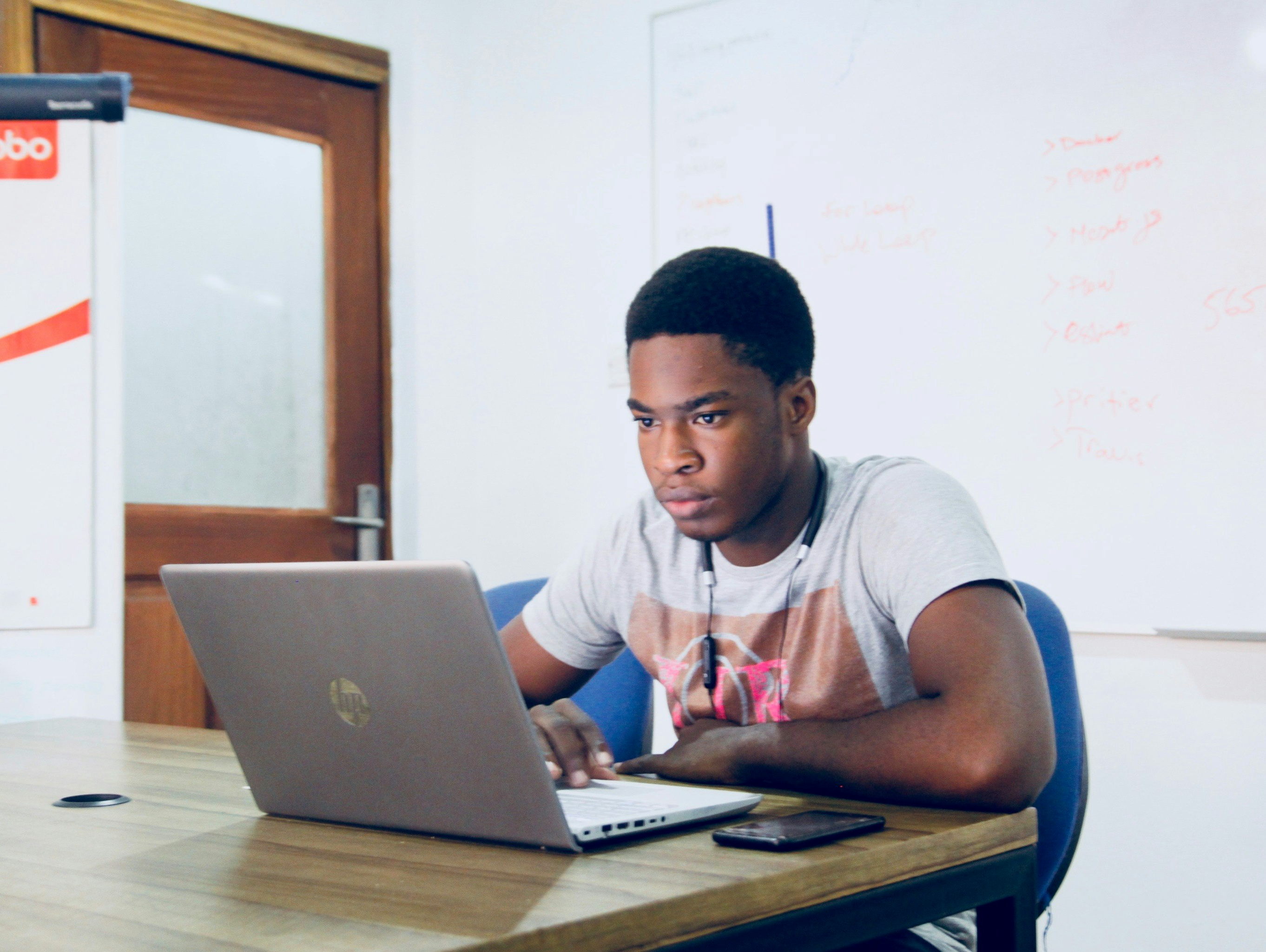 Smiling woman in white blazer working at a laptop in a modern home office setting with plants and shelves in the background.