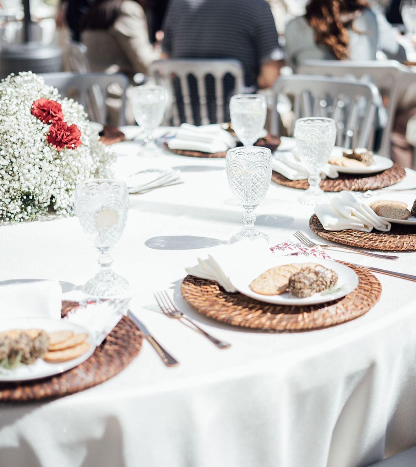 Arreglo floral de rosas rosadas en un jarrón de vidrio junto a cajas de cartón y una naranja sobre una mesa iluminada por luz natural.