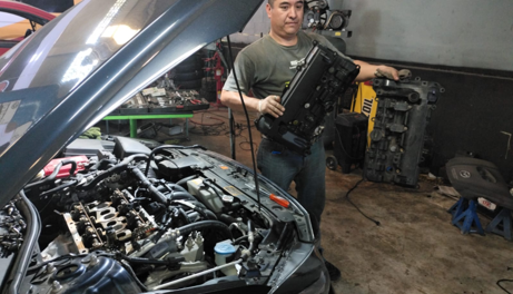 Mecánico trabajando en el motor de un automóvil en un taller, sosteniendo una pieza del motor.