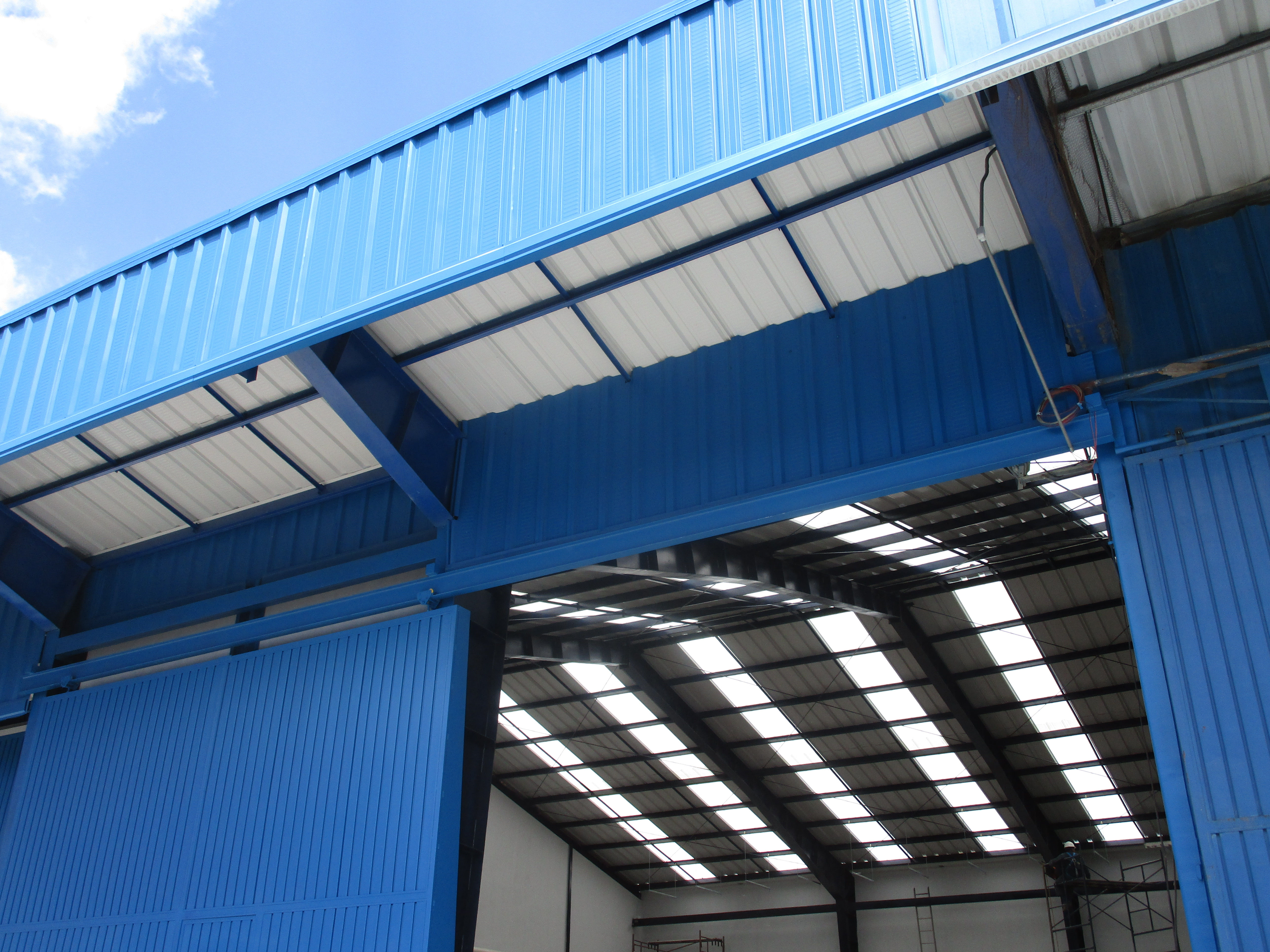 Techo y estructura de metal azul en un edificio industrial con cielo despejado.