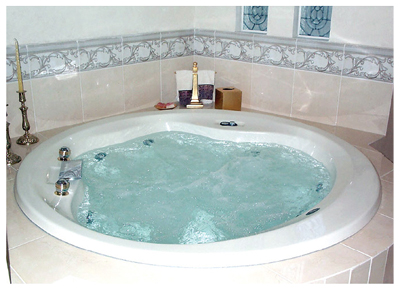 Baño minimalista con bañera blanca ovalada, espejo circular, planta en maceta y luz natural.