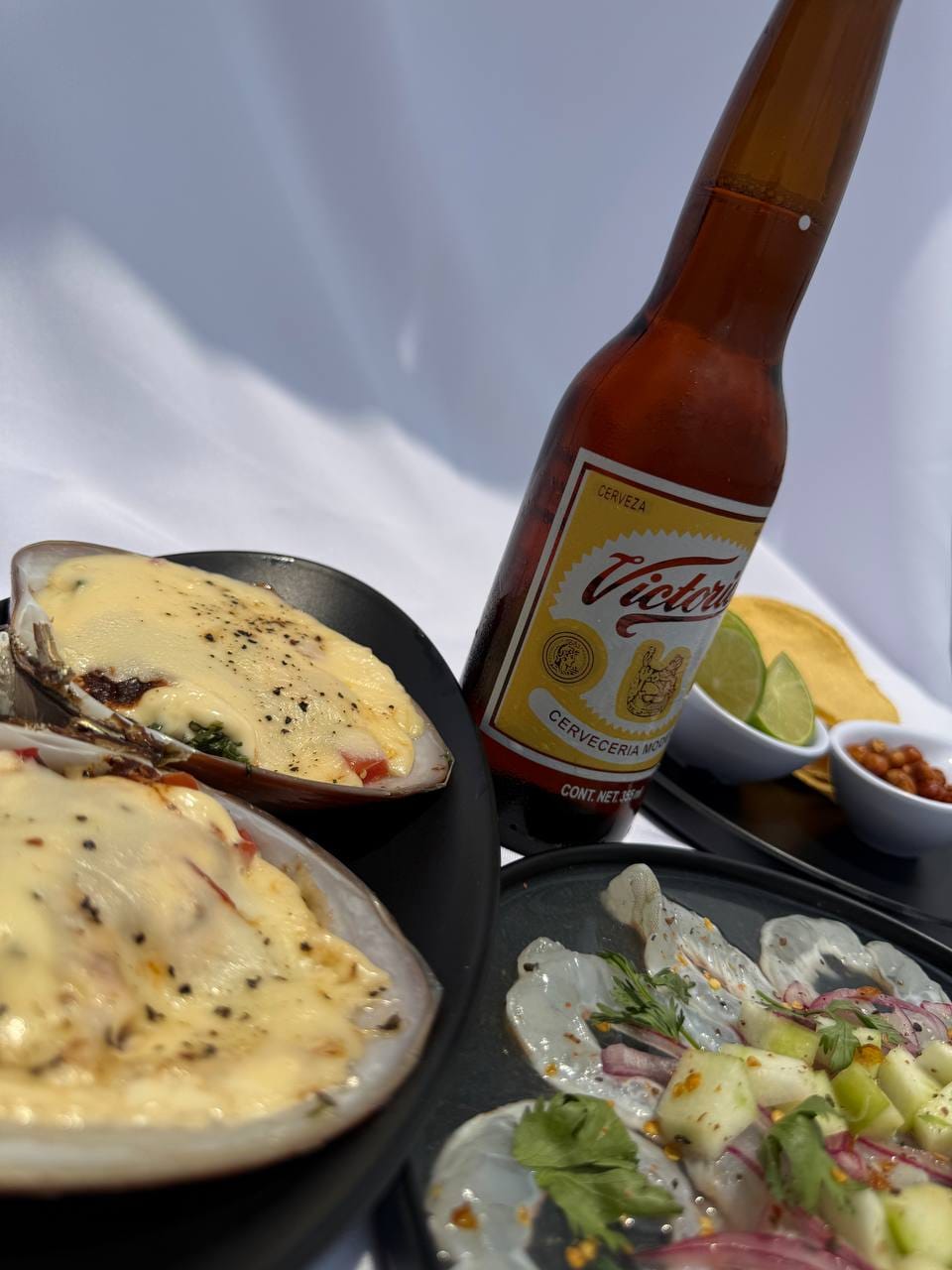Mariscos frescos con queso gratinado, ceviche y cerveza Victoria en mesa al aire libre