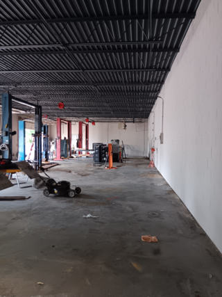 Interior of an empty industrial space with machinery, unfinished concrete floor, and metal beam ceiling.