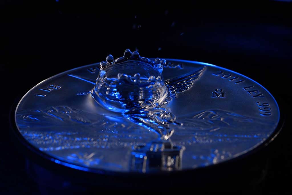 Moneda de plata iluminada con un efecto de salpicadura de agua en un ambiente oscuro.