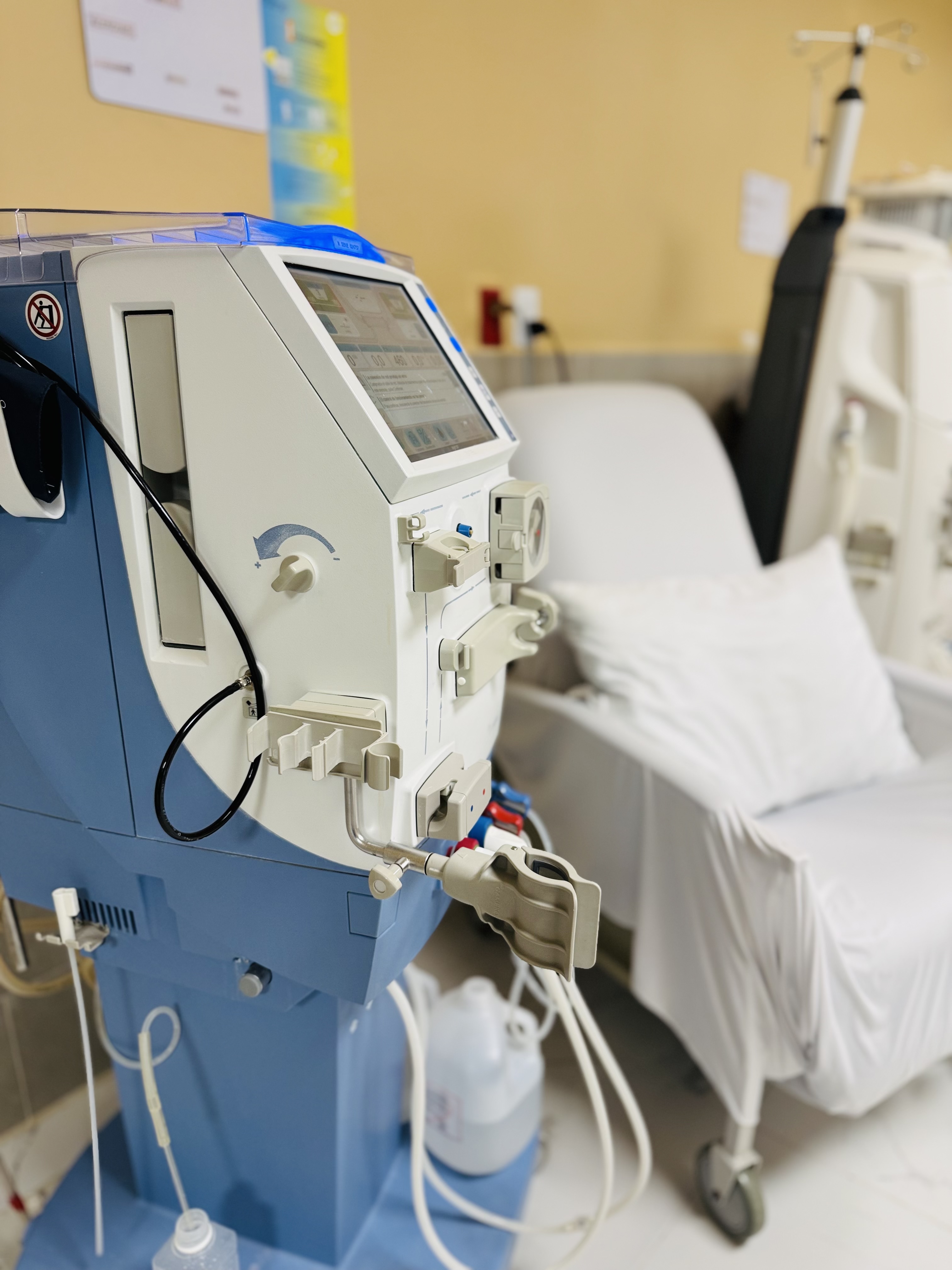 Dos profesionales médicos en una sala de hospital utilizando equipo avanzado de monitoreo médico, vestidos con uniformes azules y mascarillas, en un entorno bien iluminado.