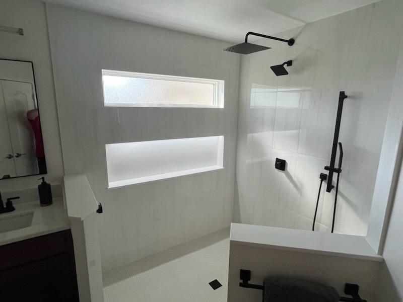 This sophisticated shower features low-voltage lighting integrated into the niche which highlights the clean feel and lines.  
The matte grey penny round shower tile adds texture and depth, while the matte black fixtures provide a bold and contemporary feel.