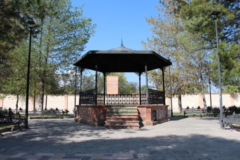 Quiosco en un parque rodeado de árboles y bancos en un día soleado.