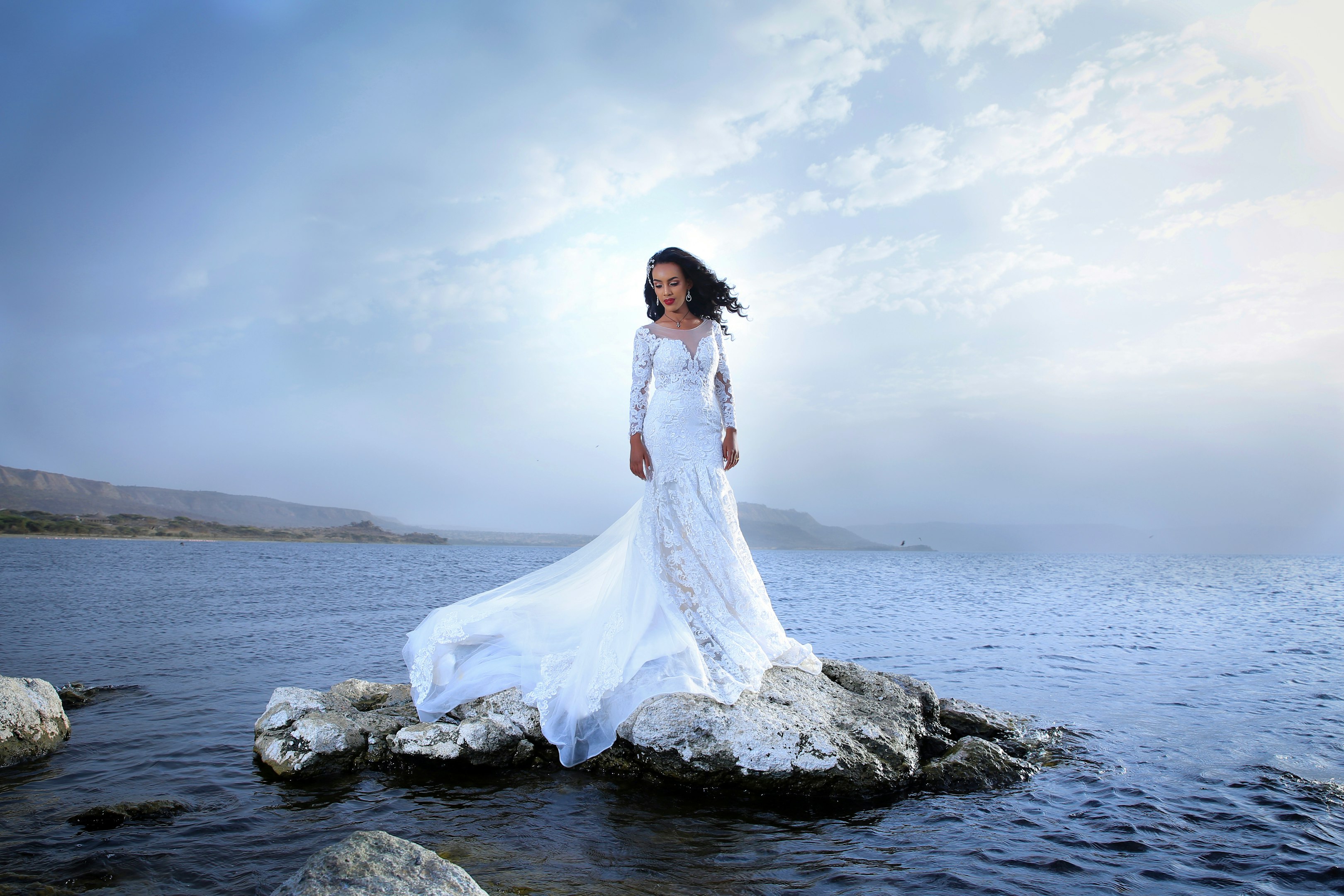 mujer con vestido blanco de pie sobre una roca cerca del mar durante el día