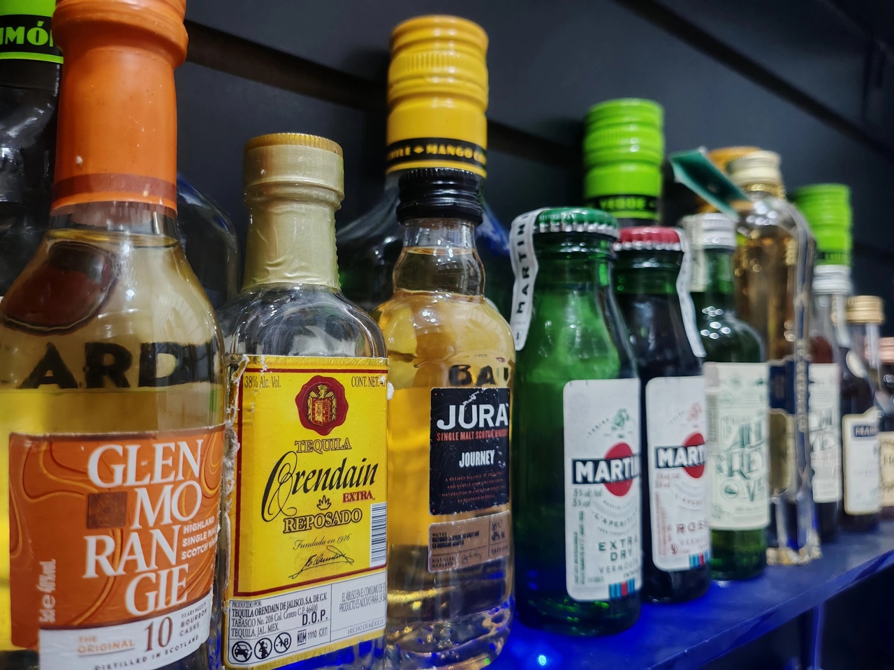 Bar moderno con estanterías de botellas, decorado con lámparas colgantes y taburetes de cuero marrón, vista urbana a través de grandes ventanales.