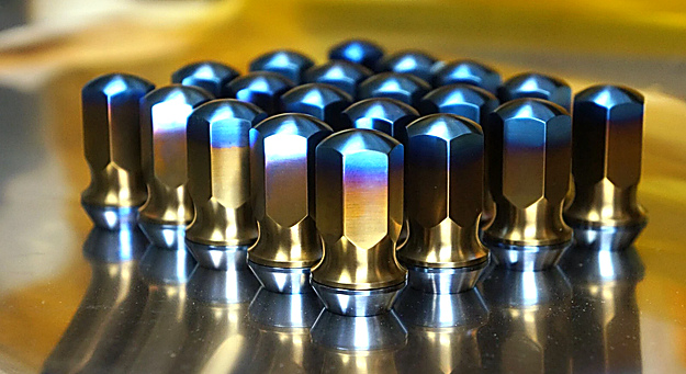 Assorted colorful titanium car wheel lug nuts and bolts displayed in front of a vehicle wheel