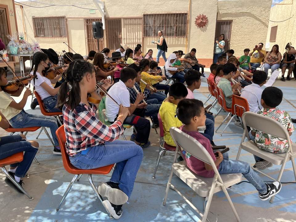 Grupo de niños con trajes tradicionales y violines en un entorno al aire libre.