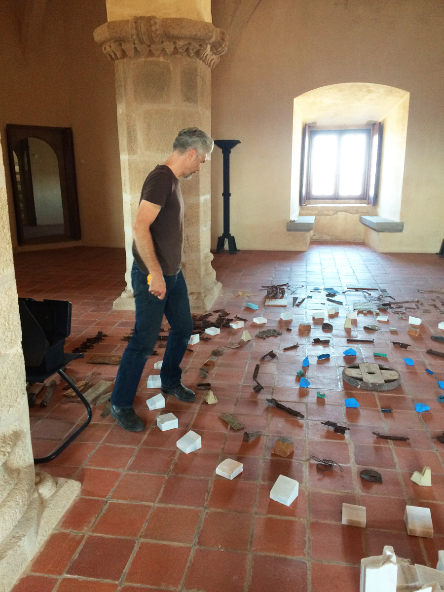 A man steps over rustic objects arranged in concentric circles on a red tile floor.
