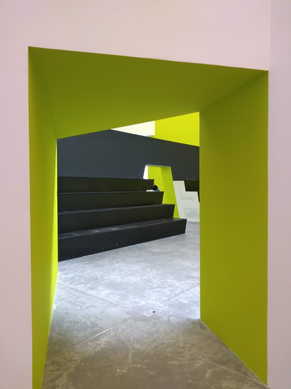 Vista de un moderno interior arquitectónico con paredes verdes y escaleras negras en un diseño geométrico.