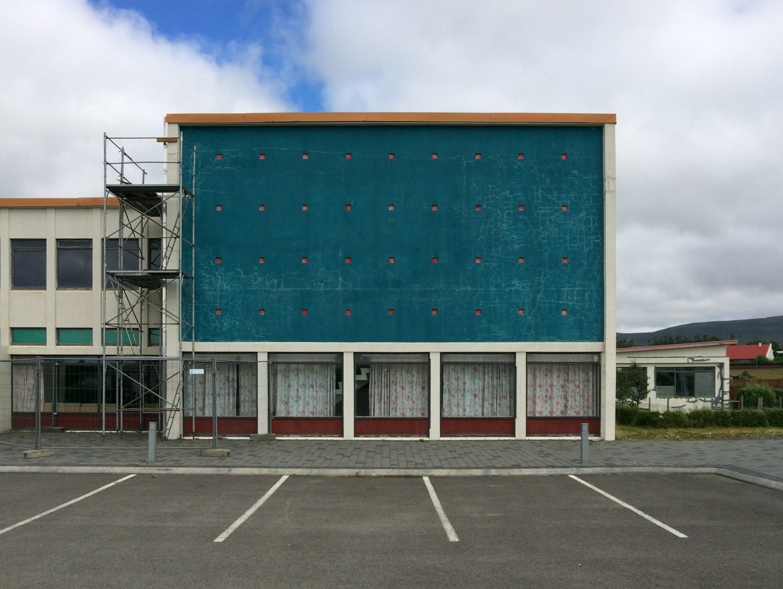 A commercial building with blank modernist turquoise facade and scaffolding.