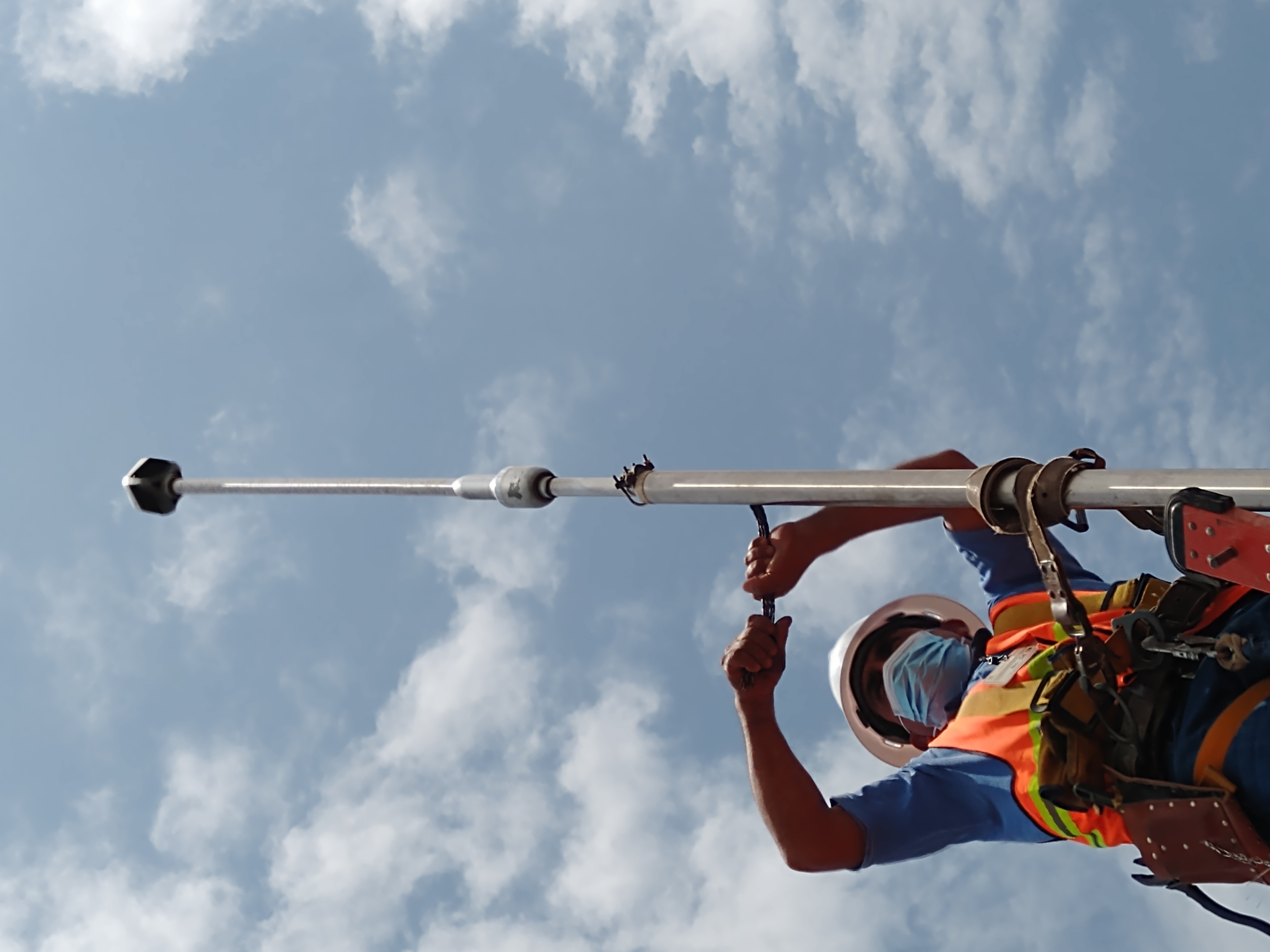 Trabajador con equipo de seguridad instalando antena en un día soleado.