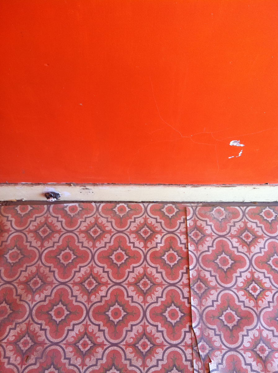 In horizontal bands, a shiny orange wall, white trim and pink patterned linoleum.