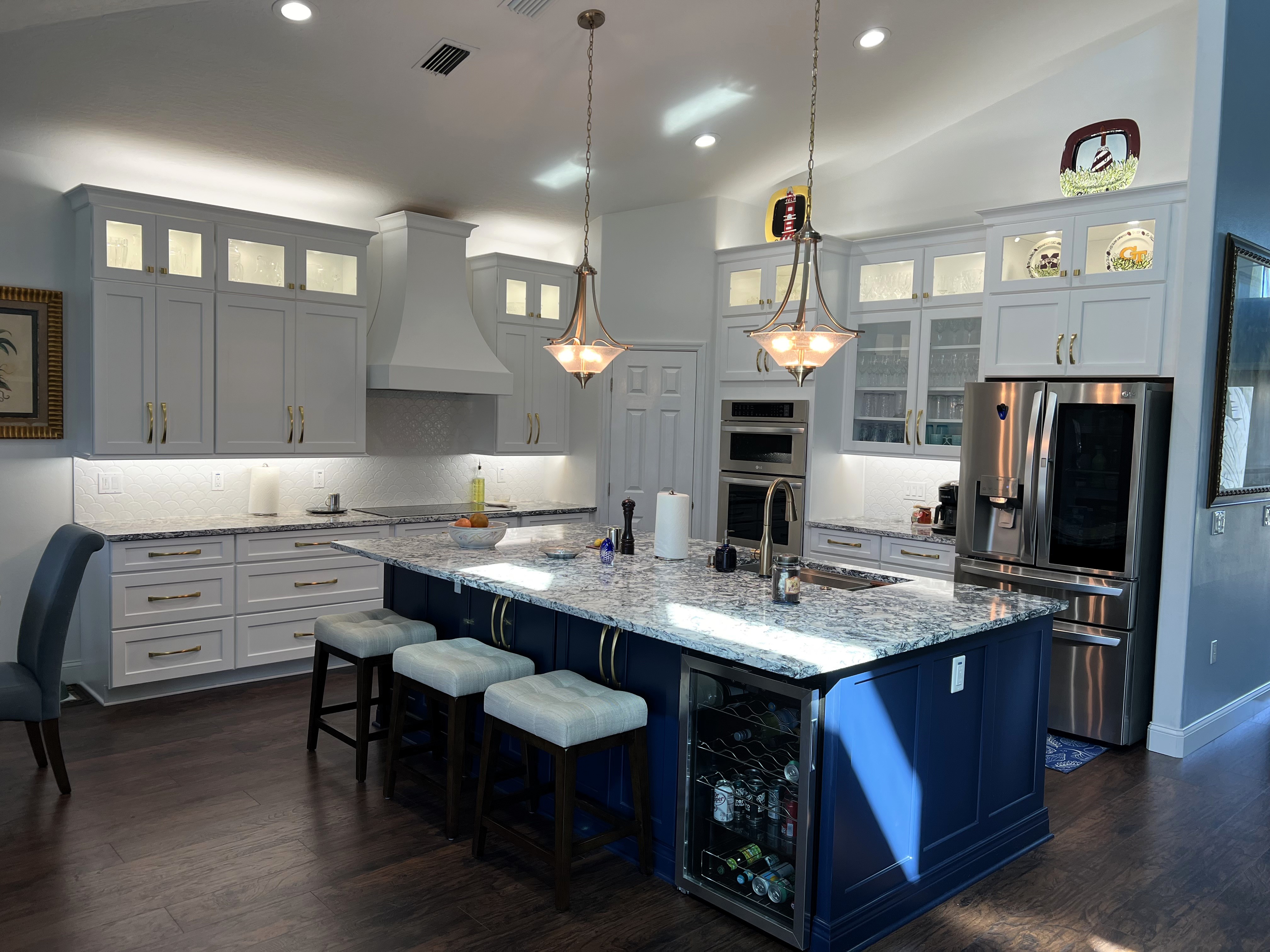 Stunning kitchen featuring semi-custom maple wood painted Sea Salt white (surround) and maple wood painted Tidal blue (island) cabinetry, with gold hardware, and perfectly laid luxury laminate flooring.